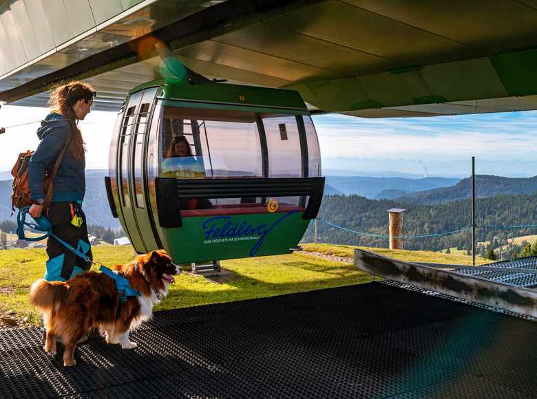 Spaziergängerin mit Hund vor einer Gondel der Feldbergbahn