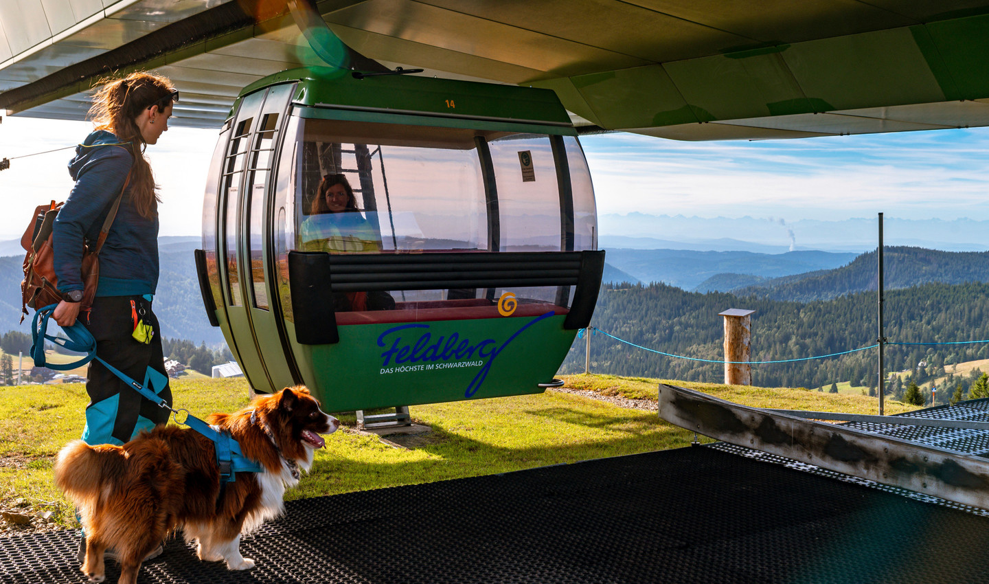 Spaziergängerin mit Hund vor einer Gondel der Feldbergbahn