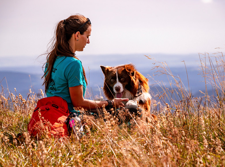 Wanderin füttert ihren Hund inmitten einer Wiese mit wundervoller Aussicht