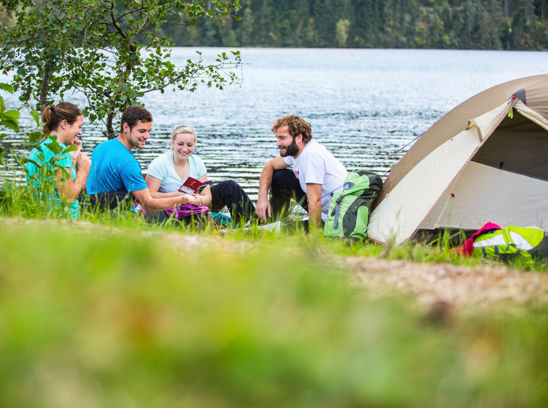 Personen sitzen gemeinsam am Ufer mit ihrem Zelt
