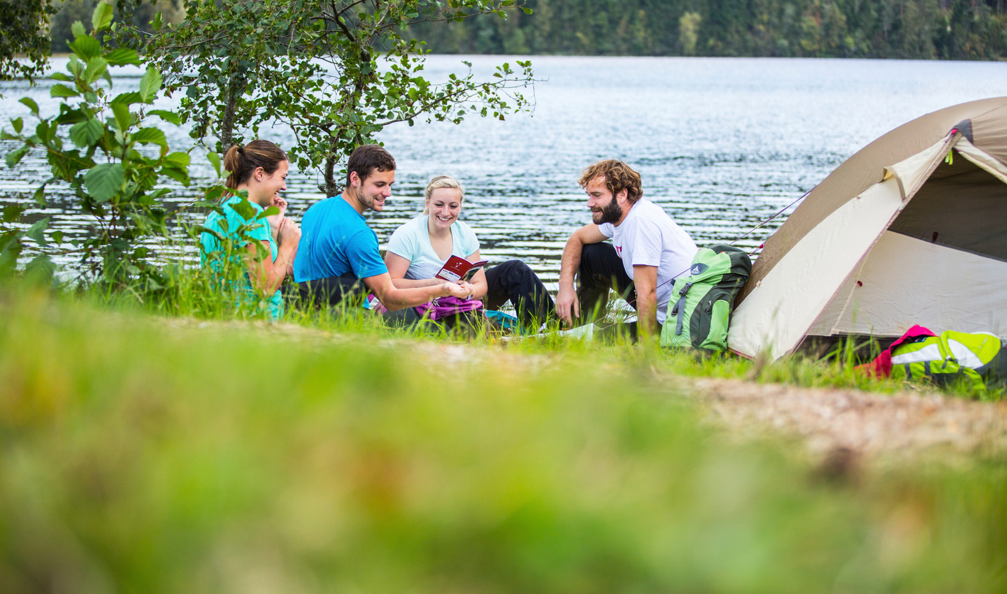 Personen sitzen gemeinsam am Ufer mit ihrem Zelt